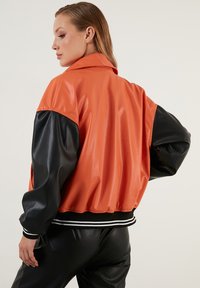 Oranje en zwarte neplederen bomberjack met een geribbelde zwart-witte zoom, met een losse pasvorm en brede mouwen.