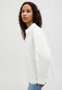 Witte langemouwen shirt met een kraag, voorzien van knoopmanchetten. Gladde katoen stof, relaxte pasvorm, gedragen over lichtblauwe denim.