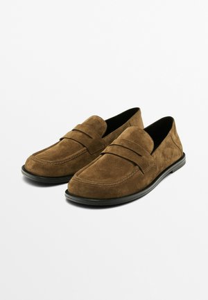 Braune Wildlederloafers mit einem niedrigen Profil, ausgestattet mit einer genähten Detailierung über dem Vorderblatt und einer schwarzen Gummisohle. Glatte Textur, minimalistisches Design.
