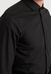 Zwarte overhemd met een gladde textuur, smalle kraag en slim fit. Heeft een klassiek ontwerp met gelijkmatig verdeelde knopen en zonder patronen.