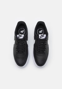 Svarta lädersneakers med vita detaljer, perforerad yta på tån, platta snören och en vit gummisula. Nike-logga på tungan.