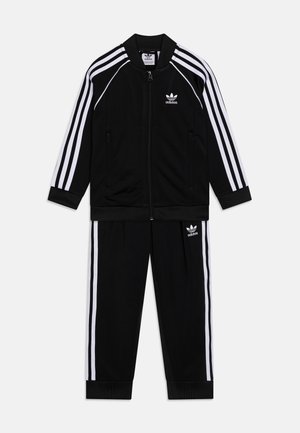 Tuta sportivo nero realizzato in tessuto morbido, con design a tre strisce bianche lungo le maniche e i lati dei pantaloni; include chiusura con zip e polsini a costine.