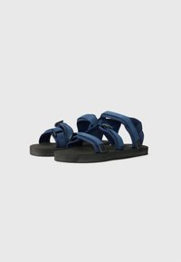 Blå stoffsandaler med flere justerbare stropper og såle i svart gummi. Har et flatt design for komfort og stabilitet.