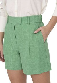 Pantalones cortos de lino verde con cintura ceñida, pinzas y bolsillos laterales, fabricados con un tejido ligero y texturizado.