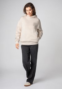 Beige fleece hoodie met een frontprint; relaxte pasvorm met een capuchon met trekkoord. Gecombineerd met donkere, losse jeans en lichte sneakers.