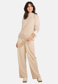 Gai bežs adīts džemperis ar brīvu piegriezumu, ribota tekstūra un dekoratīvas pogas uz pleca, kopā ar bežām platā kāju biksēm.