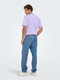 Lilla lühikeste varrukatega T-särk, mis on kombineeritud helesiniste laia lõikega teksapükstega. Teksad on klassikalise viie taskuga disainiga. Spordijalatsid on beežid.