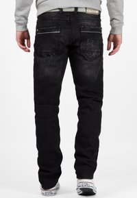 I jeans in denim nero presentano una vestibilità a gamba dritta, cuciture a contrasto e due tasche posteriori con marchio. Indossati con sneakers bianche.