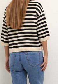 Gestreifter Strickpullover in Creme und Schwarz, mit einem lässigen Schnitt und kurzen Ärmeln; kombiniert mit hochgeschnittenen hellblauen Jeans.