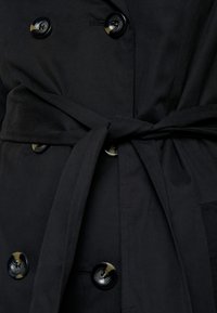 Czarny prochowiec z dwurzędowym zapięciem i dużymi, połyskującymi guzikami. Posiada materiałowy pasek i gładką fakturę.