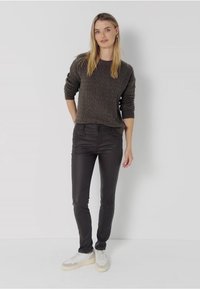 Suéter gris oscuro con un patrón texturizado, combinado con jeans negros ajustados. El modelo lleva zapatillas blancas con una suela crema.