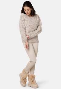 Beige gestrickter Pullover mit mehrfarbigen Punkten, langen Ärmeln und Rundhalsausschnitt; kombiniert mit cremefarbener Hose und tan-farbenen Stiefeln mit Fellfutter.
