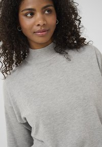 Maglione grigio chiaro a maglia con colletto alto. Presenta una texture morbida e una vestibilità ampia, caratterizzato da un design senza pattern e dettagli a coste.