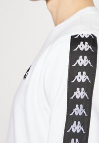 Felpa bianca con pannello laterale nero che presenta grafiche silhouette ripetute. Design a girocollo e consistenza morbida in cotone.