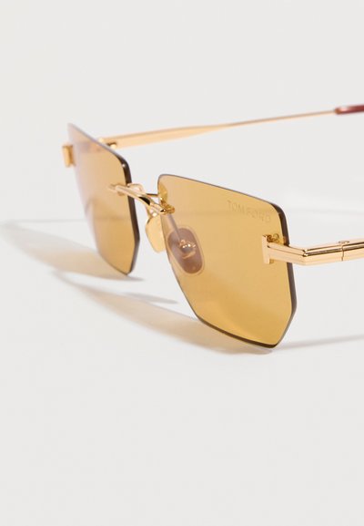 Γυαλιά ηλίου με χρυσό περίγραμμα, τετράγωνα κεχριμπαρένια φακούς και λεπτούς βραχίονες, με τη σήμανση "Tom Ford" στον δεξί φακό.
