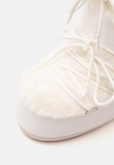 Gros plan d'une botte d'hiver blanche avec un tissu doux et duveteux sur le dessus et des lacets blancs noués en nœud.