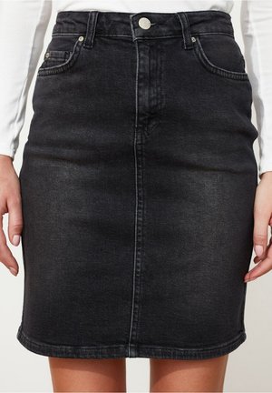 Schwarzer Jeansrock mit Frontnaht, Knopfverschluss und Taschen, getragen mit einem weißen Langarmtop bei einer stehenden Person.