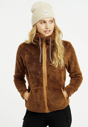 Giacca in pile marrone con colletto alto e chiusura con zip, caratterizzata da un pannello frontale a contrasto di colore tan. Accentuata da un berretto beige a coste.