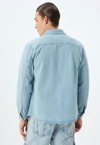 Lichtblauwe denim jacket met lange mouwen, met knopen bij de manchetten, een puntige kraag en een relaxte pasvorm. Soepele textuur met minimale stikseldetails.