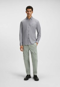Camisa gris de botones con cuello, combinada con pantalones cargo verde claro con bolsillos laterales y botas negras con cordones.