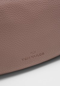 Sac à main en cuir de couleur blush doux, avec une surface texturée et un logo embossé. Design durable et bien conçu avec des bords lisses.