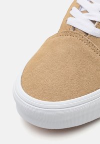 Tan suede sneaker met een ronde neus, witte gestructureerde rubberen zool en platte witte veters. Het bovenwerk heeft een gladde en zachte textuur.
