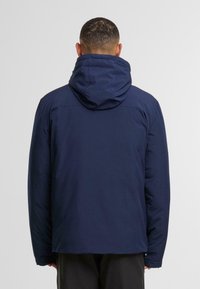 Donkerblauwe, capuchonjack met een stevige textuur, ruime pasvorm en een rechte zoom. Het heeft lange mouwen en subtiele stikdetails op de achterkant.