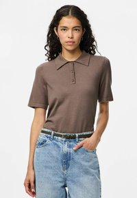 Brun stickad polo skjorta med korta ärmar och krage, med tre knappar. Kombinerad med högmidjade ljusblå jeans och ett grönt bälte.