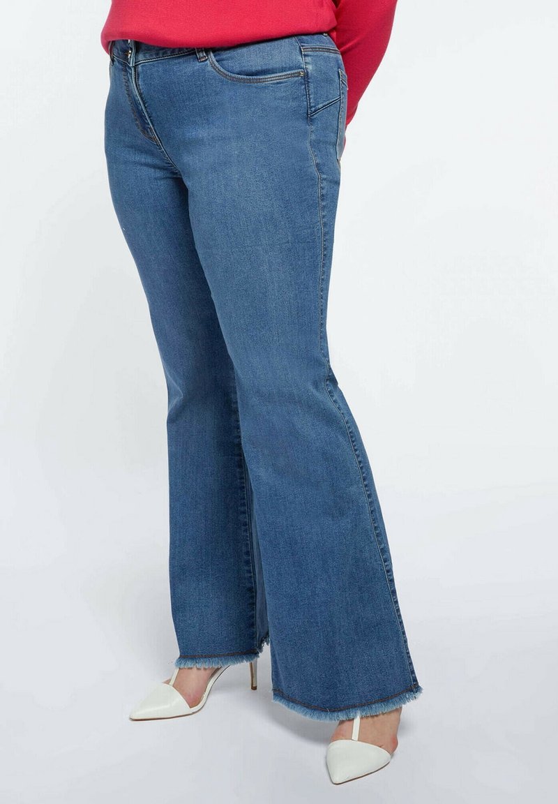 Džíny s rozšířenými nohavicemi v středně modré barvě, s nezačištěným lemem, standardními kapsami a obepnutým pasem. Stylizováno s bílými lodičkami s špičatou špičkou.