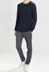 Navy cable-knit sweater with ribbed cuffs and hem, paired with gray slim-fit pants and white sneakers. Simple, casual ensemble.