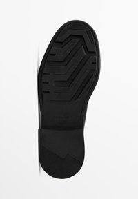 Semelle de chaussure noire avec un motif texturé, incluant des lignes et des crêtes pour une meilleure adhérence. Présente un talon lisse et arrondi ainsi qu'un logo de marque.