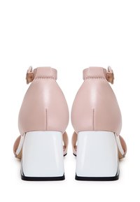 Sandales à talons hauts en cuir rose avec un solide talon bloc blanc, des brides autour de la cheville, et un design ouvert avec un bout arrondi et une esthétique minimaliste.