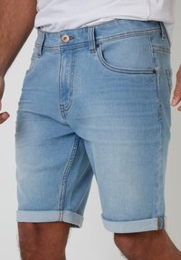 Pantalones cortos de mezclilla azul claro con dobladillos enrollados, que cuentan con cinco bolsillos, cierre de botón y un ligero desgaste para un look casual.