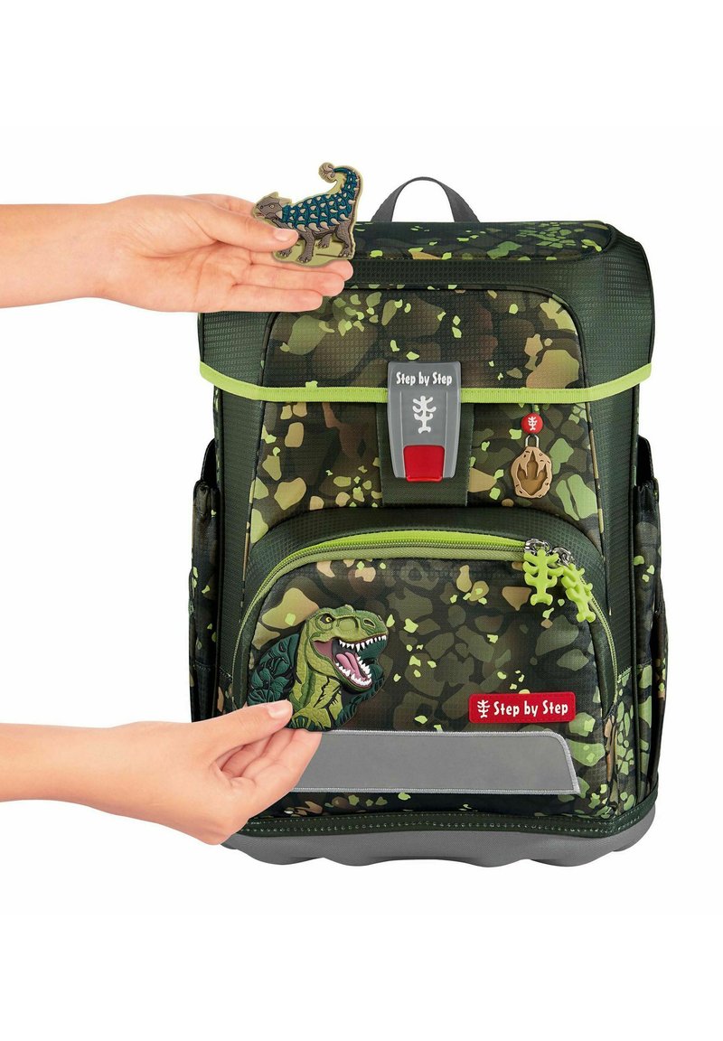 Sac à dos à motif camouflage vert avec des accents gris. Comprend des badges amovibles sur le thème des dinosaures et une sangle réfléchissante à l'avant.