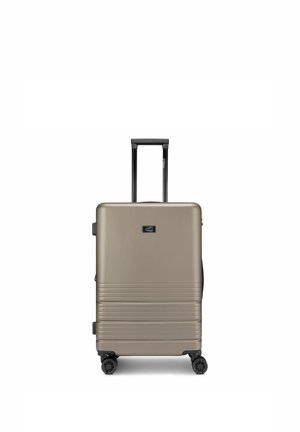 Piccola valigia rigida beige con quattro ruote girevoli e manico telescopico esteso, vista frontale su sfondo bianco.