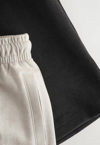 Sorte og cremefarvede joggingbukser med elastisk talje og sidelomme, lavet af glat, blødt stof med kontrasterende farver.