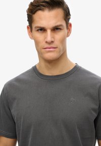 T-shirt in cotone grigio con maniche corte, collo rotondo e un piccolo logo ricamato sul petto. Tessuto morbido e vestibilità casual.