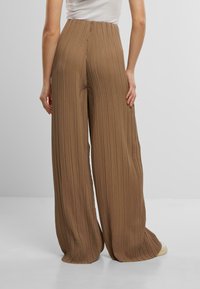 Bruine plissé wijde broek met hoge taille. De stof heeft verticale groeven en biedt een zachte textuur. Geen zichtbare hardwaredetails.