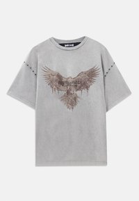 Grijze oversized t-shirt met een vervaagde adelaarafbeelding en de tekst "JUST CAVALLI." Heeft studs langs de mouw voor extra detail.
