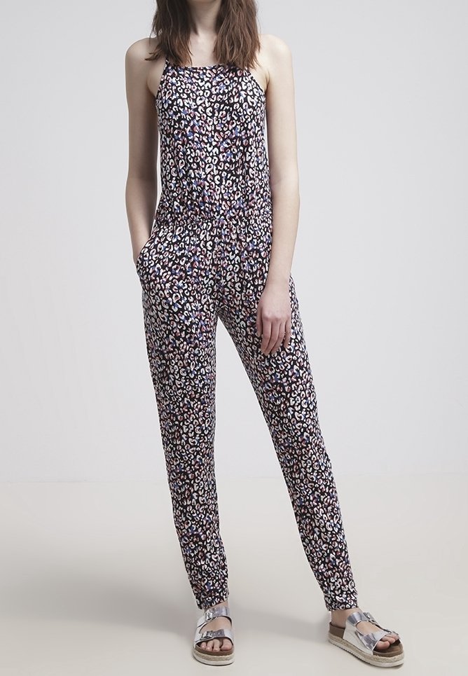 Mono negro con un patrón de leopardo en rosa, morado y blanco. Presenta tirantes finos, una cintura elástica y bolsillos laterales. Sandalias plateadas.