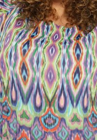 Blouse multicolore présentant un motif abstrait vibrant avec des vagues de violet, vert, bleu et orange. Tissu léger avec des plis.