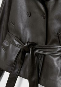 Čierna kožená bunda s dvojradovými gombíkmi, prednými vreckami a širokým opaskom zviazaným uzlom v páse.