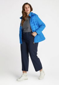 Giacca blu imbottita con cappuccio, pantaloni blu scuro e sneakers bianche. La giacca presenta una texture trapuntata; la parte superiore ha strisce blu scuro e bianche.