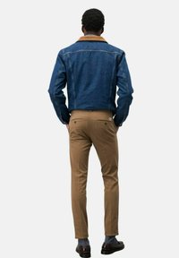 Giacca di jeans con colletto marrone, di colore blu e dettagli cuciti, abbinata a pantaloni marroni chiari e scarpe scure. Vista dal retro.