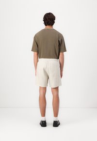 Kortermet, olivengrønn bomull T-skjorte kombinert med lysebeige linshorts, med elastisk midje og baklomme. Svarte sko og hvite sokker.