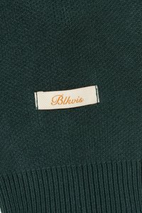 Green knitted fabric with ribbed texture, featuring a cream label with the text "Blkvis" in orange.