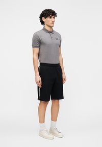 Pilkas polo marškinėlis trumpomis rankovėmis ir apykakle; juodi šortai su šoninėmis juostelėmis; smėlio spalvos sportiniai bateliai; balti kojinės iki kulkšnių. Paprastas sportinis aprangos komplektas.