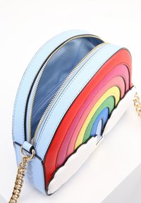 Pieni olkalaukku, jossa on sateenkaaren kaaret ja valkoiset pilviakcentit, vaaleansiniset sivut, kultainen vetoketju ja ketjusolki, laukku osittain auki.