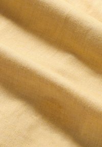 Jasnożółty materiał, teksturowany delikatnym żebrowaniem. Tkanina wydaje się miękka i gładka z subtelnym połyskiem, układając się w łagodne fałdy.