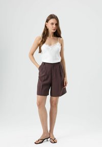 Witte camisole met kanten afwerking gecombineerd met hoge taille, donkerbruine shorts. Schoeisel: zwarte minimalistische sandalen. Eenvoudig, aansluitend ontwerp.